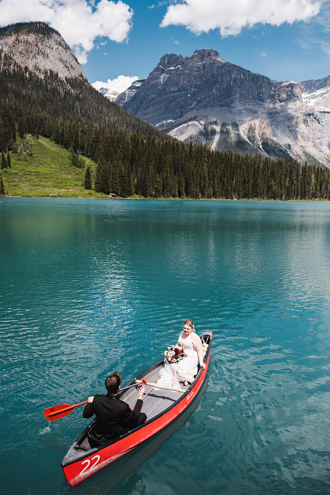 Bride and groom paddling a red canoe across the turquoise water of Emerald Lake