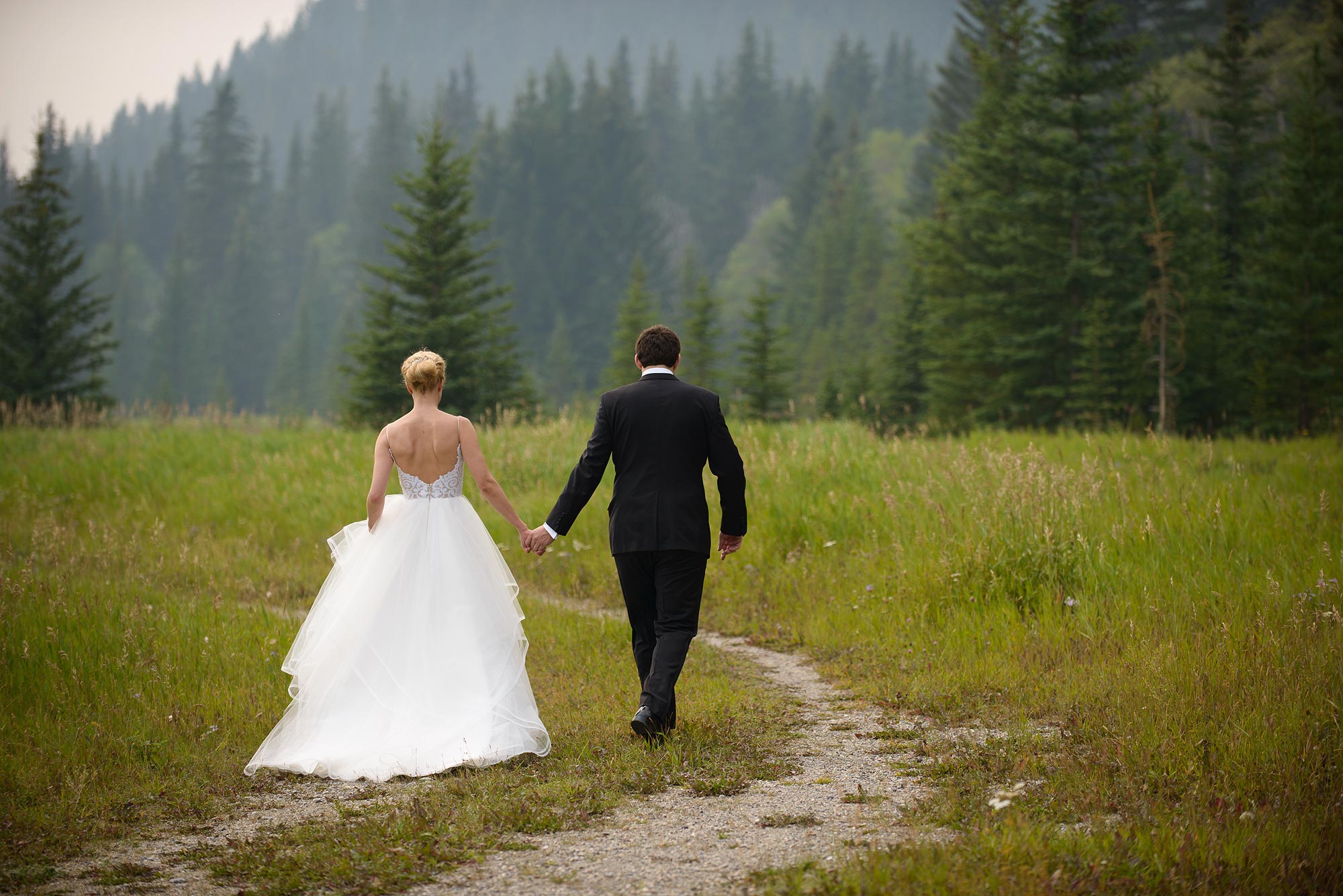 Couple walking through a mountain meadow toward evergreens in Banff
